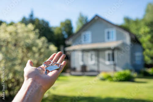Hand holding house keys in front of blurred home