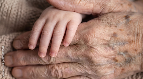 Close up of an elderly person holding the hand of a newborn baby with connection
