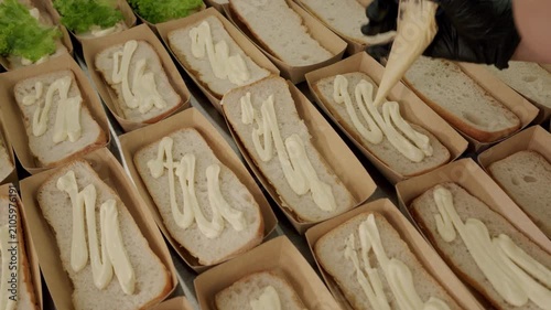 Preparation of sandwiches with fresh lettuce and mayonnaise spread on bread in a clean kitchen setting, showcasing the assembly process in a food preparation area
