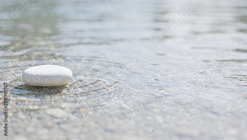 A smooth white stone resting in shallow clear water with circular ripples