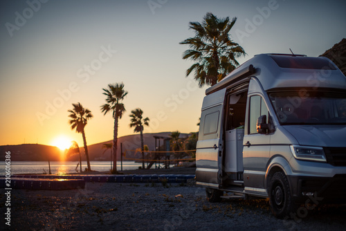 Campervan parked beside a palm-lined beach at sunset