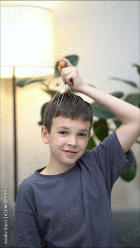 Cheerful boy enjoys scalp massage with a head massager, looking happy and relaxed.
