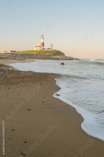 Waves washing onto a sandy beach with Montauk Point Lighthouse in the distance at the eastern tip of Long Island, New York