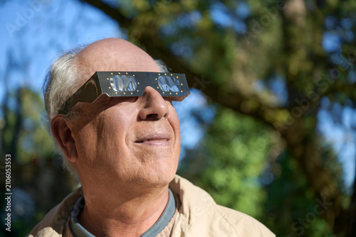 Obraz na plátně Elderly Gray Haired Man Protecting Eyes with Solar Eclipse Goggles while looking