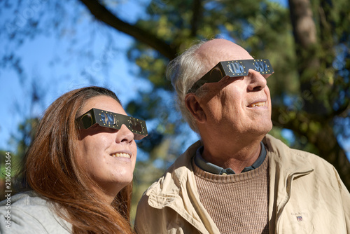 Bild auf Leinwand Smiling Woman and Retired Man Using Special Solar Eclipse Goggles at Sunset whil