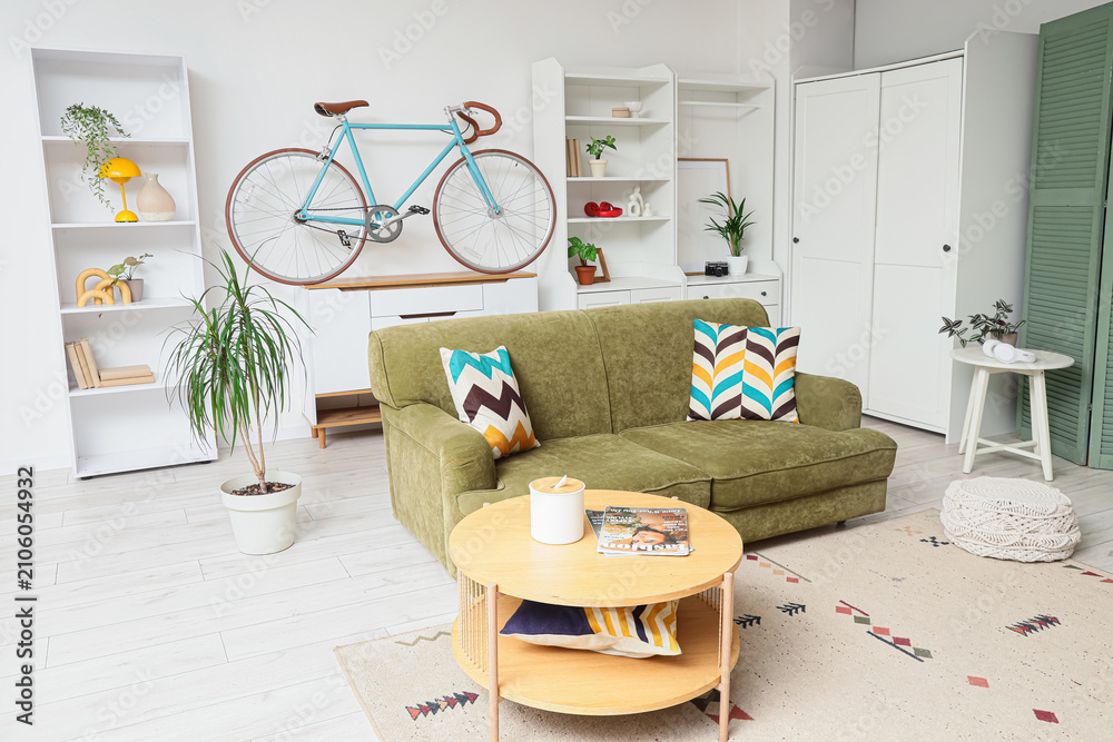 Obraz premium Modern living room interior with a green sofa, wooden coffee table, and a bicycle mounted on the wall