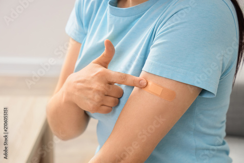 Fotografie Woman pointing at a medical plaster on her arm after vaccination, health care an