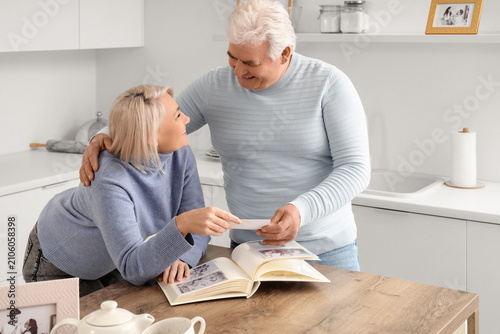Senior couple with photo album at table in kitchen. Memories concept