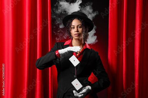 Fotografie Young African-American magician showing magic trick with flying cards near red c