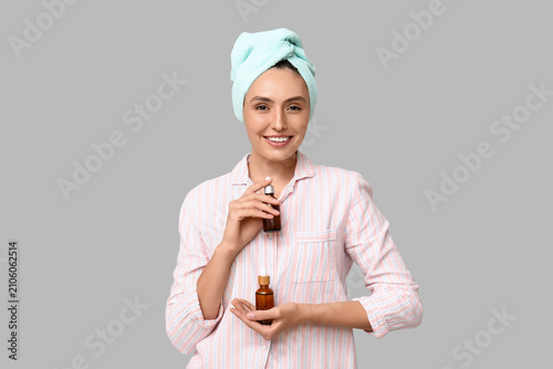 Young woman with cosmetic dropper bottles on light background