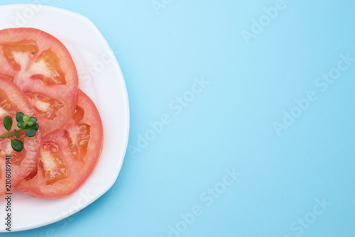 Fresh sliced tomatoes on white plate over blue background