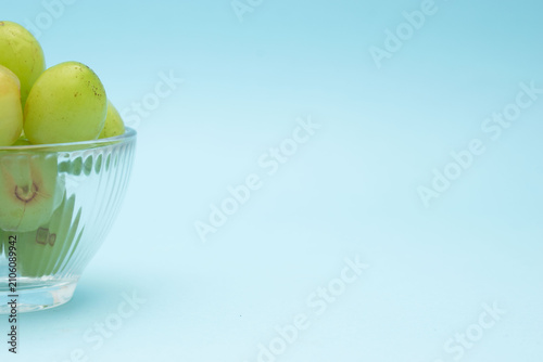 Green grapes in glass bowl on blue background with copy space