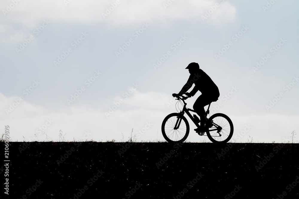 Obraz premium High-contrast profile silhouette of a cyclist riding a bicycle along a hilltop trail under an expansive sky illustrating outdoor recreation active transportation fitness eco-friendly commuting and