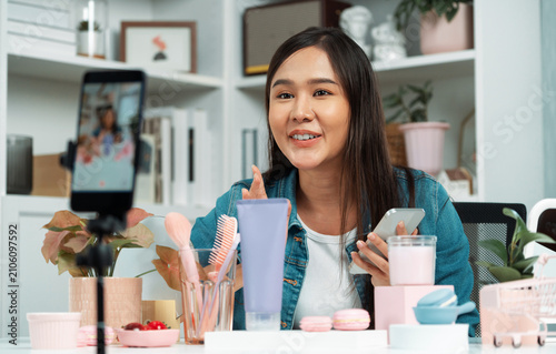 фотографія Young beautiful Asian reviewing cosmetic makeup and skin care collection, talking customer on social media online, presenting product surrounded beauty merchandise recording blurred phone