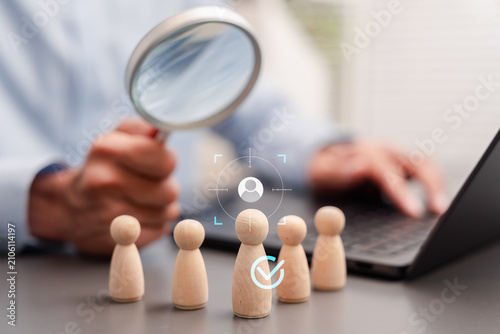 Human resources and selective hiring concept. Businessman choosing the best candidate from wooden figures with target overlay.