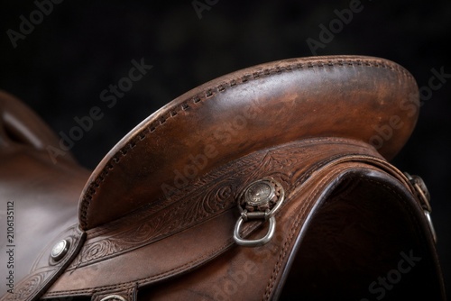 Close-up of a western saddle's leather cantle with metal fittings on dark background.