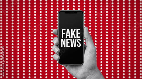 Hand holding smartphone displaying fake news text against red background