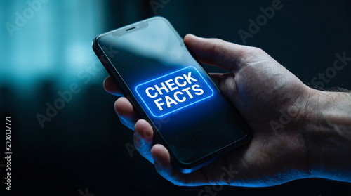 Hand holding smartphone displaying glowing check facts text on screen
