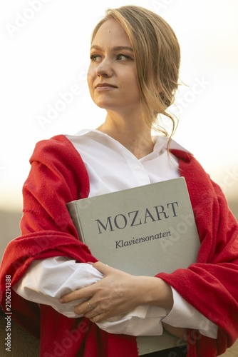Self-confidently looking young woman, pianist, in white blouse and red cardigan, in the evening light, holding notes with Mozart, piano sonatas, in her arms, Stuttgart, Baden-Württemberg, Germany