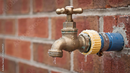A brass outdoor water faucet leaking drops on a red brick wall background