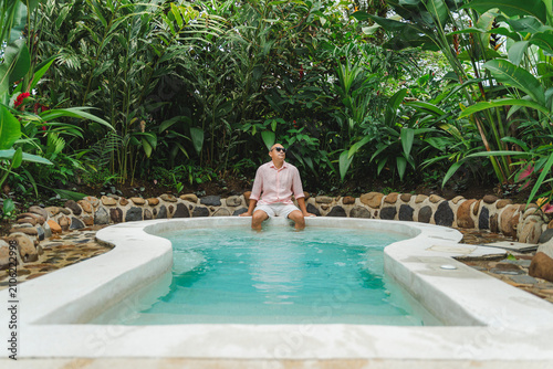 Quadro su tela Man relaxing in pool immersing feet on tropical vacation