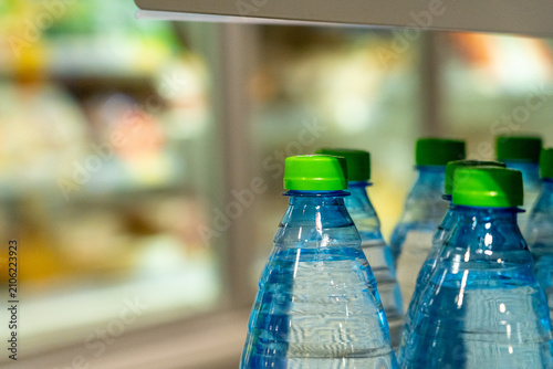 A Close-Up View of Bottled Water with Green Caps in a Chilled Display, Showcasing Refreshing Beverage Options Against a Blurred Refrigerated Background.