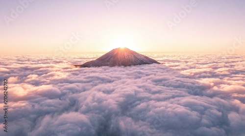Majestic mountain peak emerging from a sea of clouds during a soft sunrise
