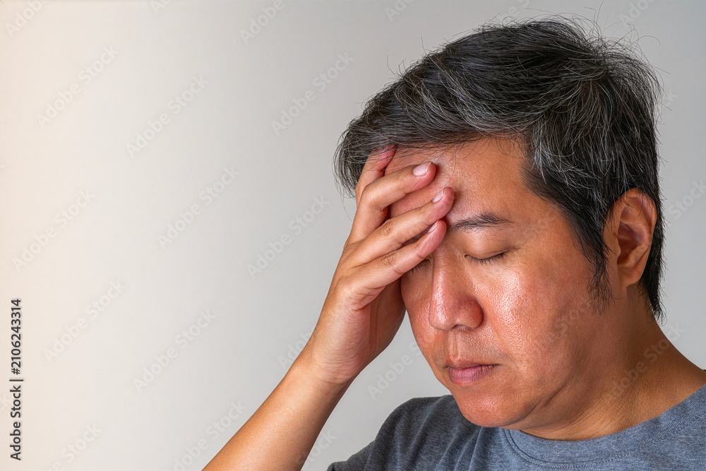 Fototapeta premium Elderly man pressing forehead, eyes closed in pain, plain background highlights dizziness and medical recovery theme.