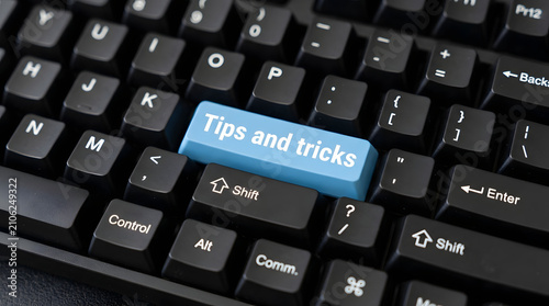 Blue key labeled tips and tricks on black computer keyboard with displays close black reading tips information technology education equipment