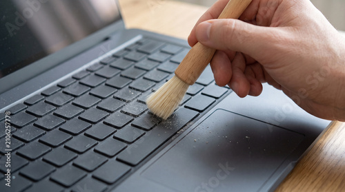 Person cleaning laptop keyboard with brush. Maintenance of modern computer hardware.