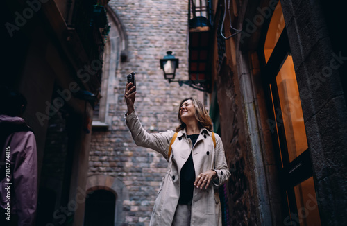 фотографія Mature woman traveler taking photo with smartphone in historic city alley