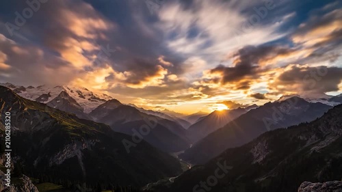 Sunlight streams over the majestic peaks of a vast alpine mountain range