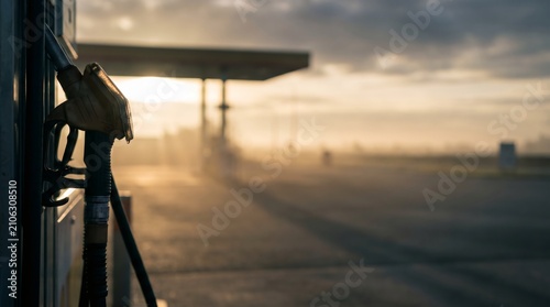 Gas pump nozzle in focus at service station during foggy sunrise, transport fuel and morning commute concept