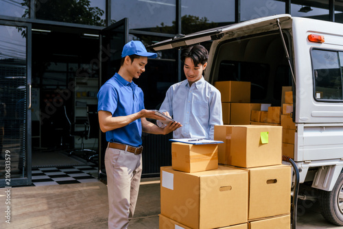 Two delivery workers checking paperwork beside a van loaded with cardboard boxes outside a building