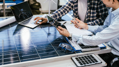 Business team discussing solar power project around a desk with solar panels, laptop, tablet and documents in an office meeting