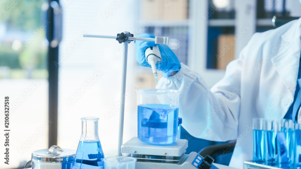 Fototapeta premium Scientist in lab coat and gloves using a pipette with blue liquid in a modern laboratory setting.
