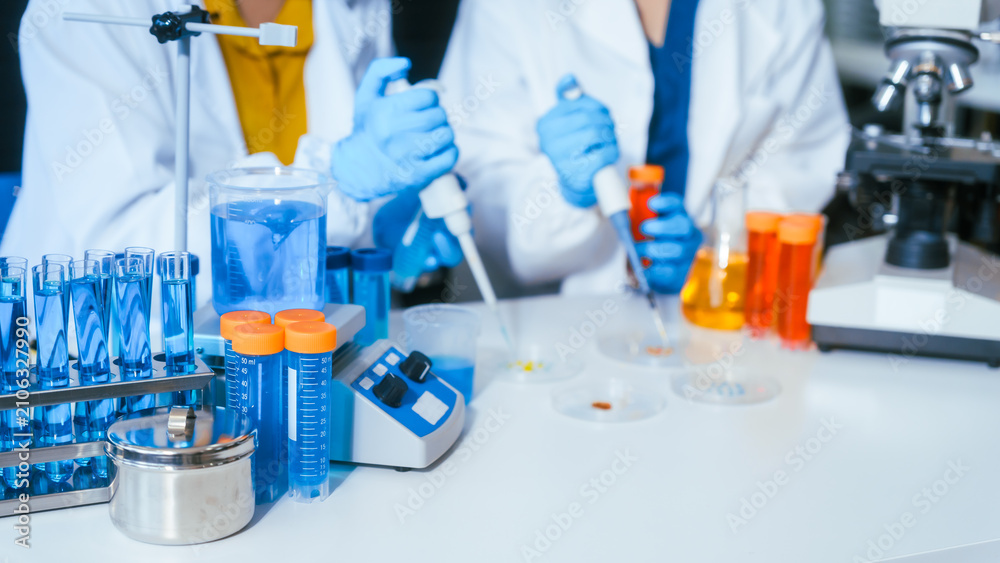Fototapeta premium Scientists working with test tubes and pipettes in a modern laboratory with glassware, blue gloves, and medical research equipment on a clean desk