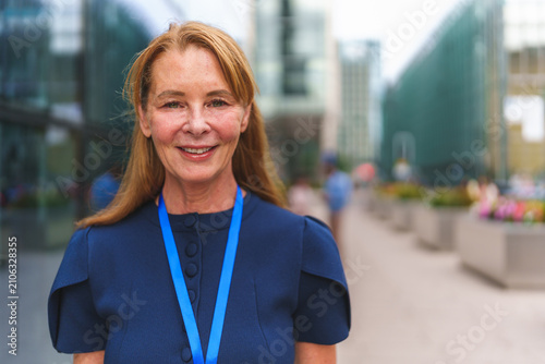Foto Senior businesswoman smiling, wearing a blue dress and lanyard outside an office
