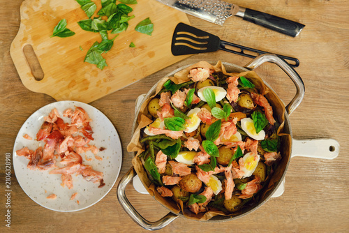 Top view of pot with smoked pink salmon salad with potatoes and fresh basil in kitchen