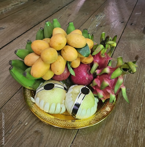 Isolated golden tray of auspicious mixed fruits including banana, marian plum, pear, and dragon fruit for Chinese New Year offering on wooden background