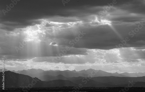 panoramic black and white photo of striking sunset with crepuscular rays over  the boulder flatirons and the front range of the colorado rocky mountains, as seen from broomfield, colorado