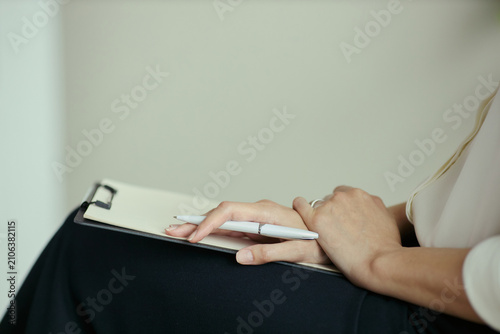 Close up of young woman holding pen over clipboard while waiting or listening  suggesting consultation or assessment. Ideal for therapy  coaching  intake  counseling marketing