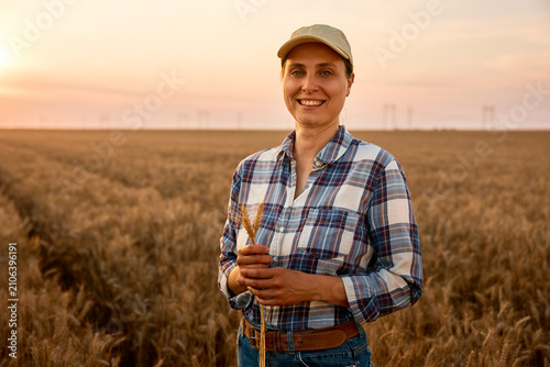 Female farmer holding wheat in a golden field at sunset