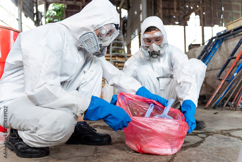 Close-up of professional hazmat workers safely packing contaminated waste into a hazard bag after a chemical spill cleanup in a manufacturing plant, ensuring corporate safety compliance.