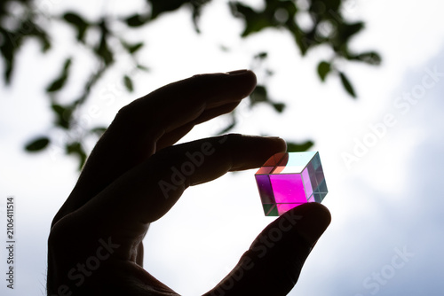 фотографія Hand gently holds a dichroic glass cube glowing magenta and teal against the sky