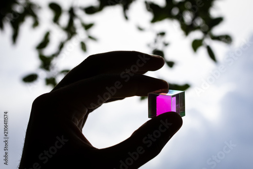 Konstfotografi Silhouette of a hand presenting a colorful prism cube before a cloudy sky hintin