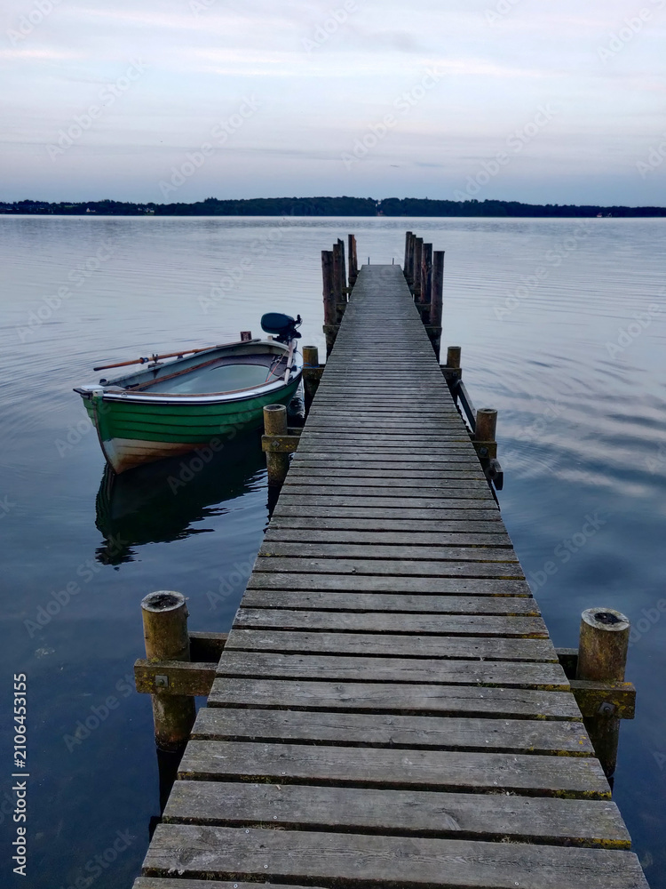 Fototapeta premium A wooden pier extends into a calm lake with a small boat tied to its side.