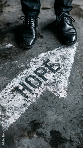 A Path of Hope: A person stands at the edge of a chalk-drawn arrow on a rough surface, with the word HOPE clearly marked, symbolizing a direction towards optimism and new beginnings.
