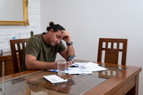Worried man calculating finances with bills and smartphone