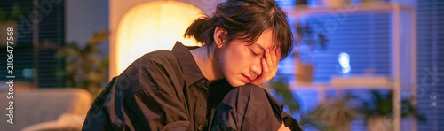 Struggling Under Pressure: A young person appears exhausted and overwhelmed, head in hand, as they face a difficult task in a dimly lit room, conveying a sense of stress and emotional strain.